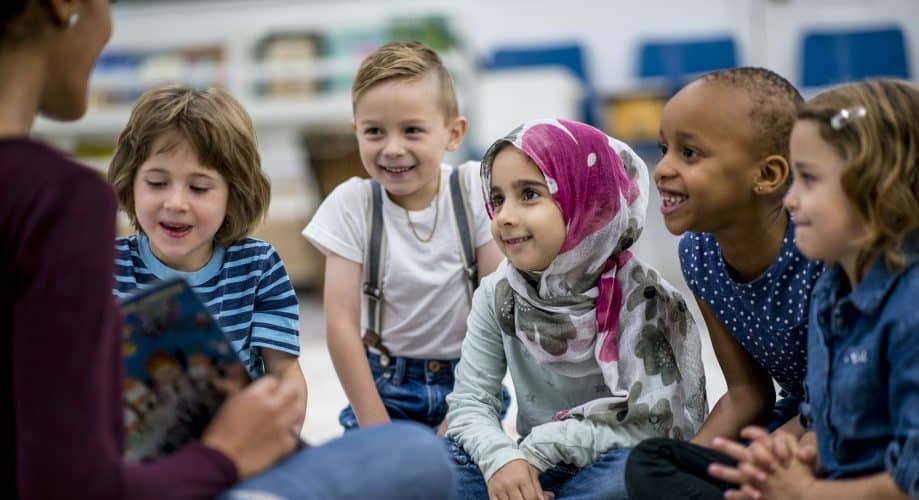 diverse preschool class listening to a book read by their caregiver