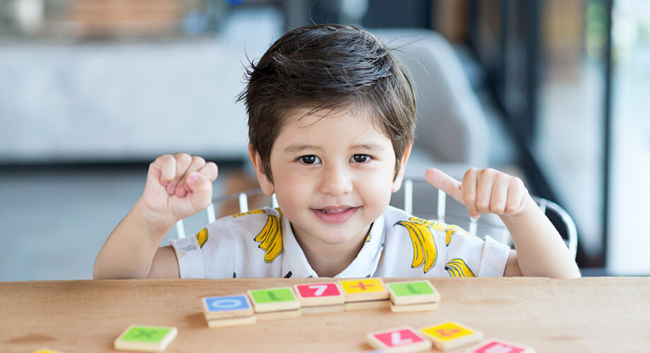 Young child practicing early math, science and engineering with number tiles in preschool room